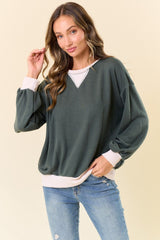 woman wearing an oversized dark green sweatshirt with white ribbed details and puff sleeves paired with light blue jeans