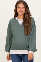 woman wearing a green maternity sweatshirt with a white hem and v-neckline, showing her baby bump