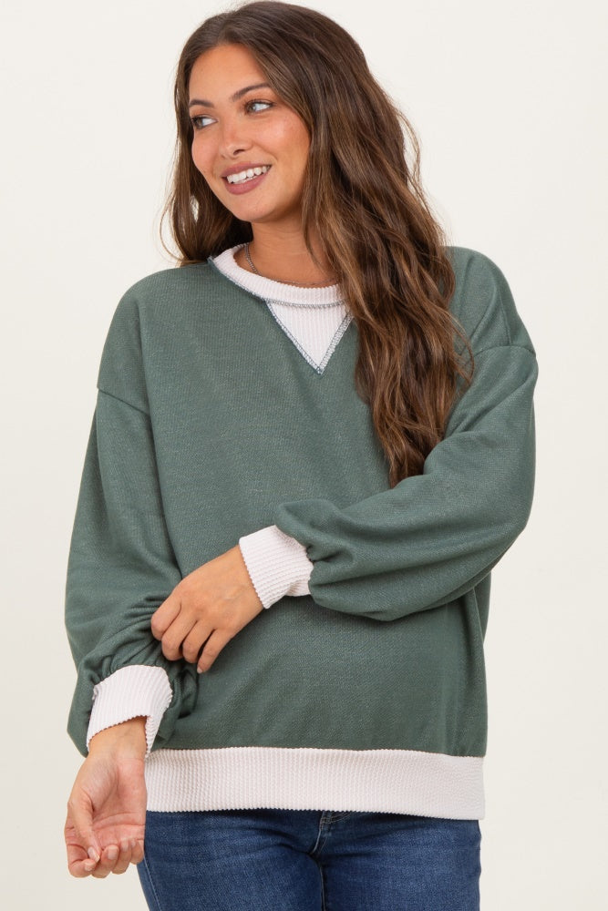 woman wearing a green maternity sweatshirt with white trim and a visible baby bump