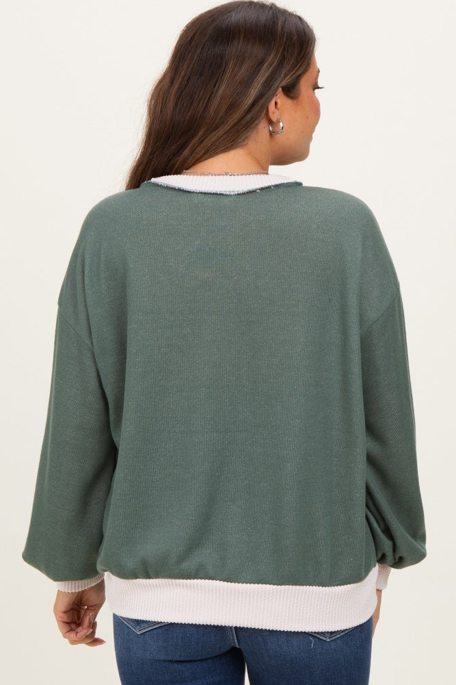 woman wearing a green oversized maternity sweater with a white hem, showing her baby bump from the back