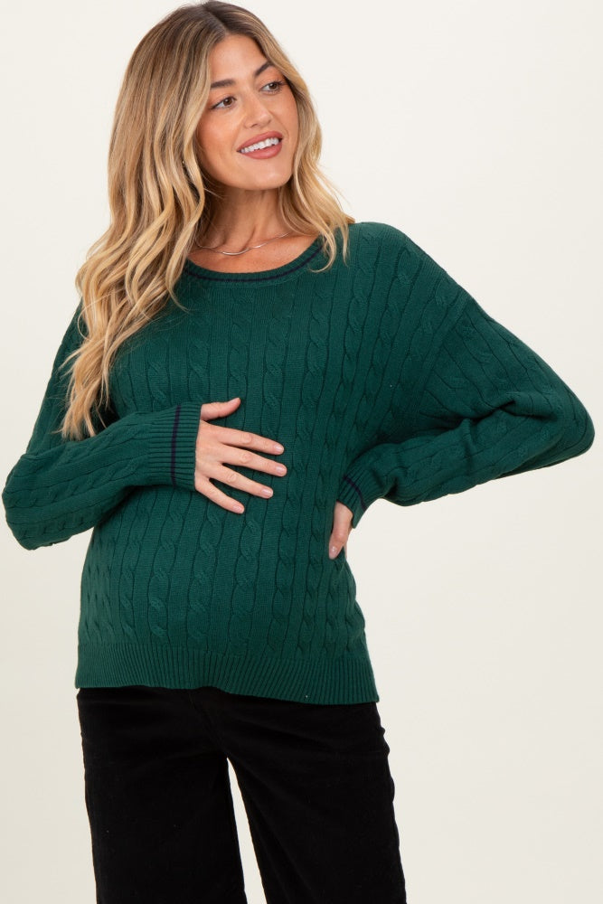 woman wearing a green cable knit maternity sweater and holding her baby bump