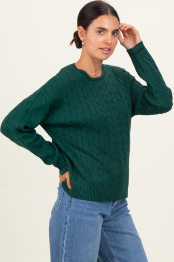 woman wearing a green cable knit sweater with a round neckline and relaxed fit, paired with blue jeans
