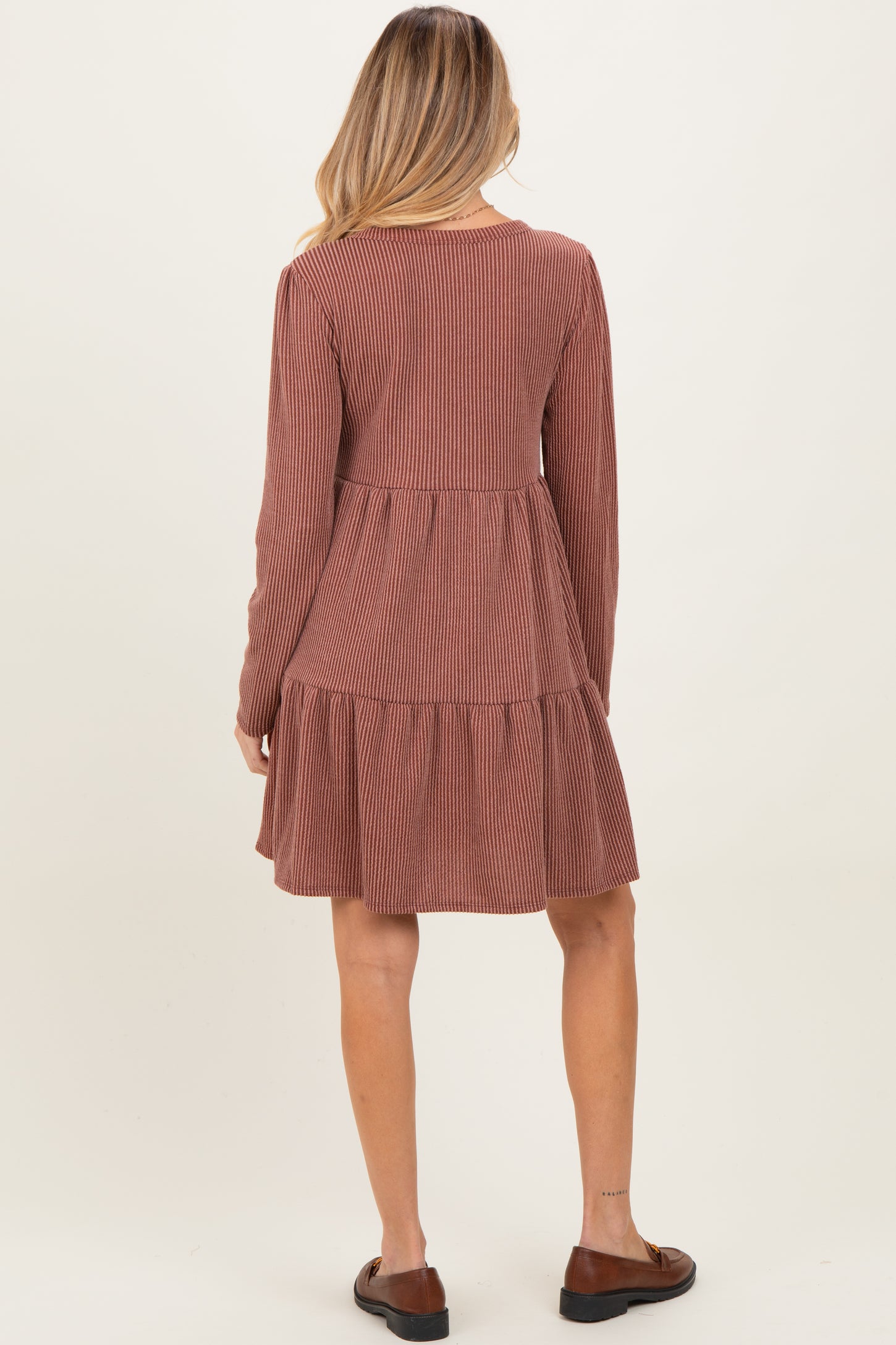 woman wearing a rust colored corduroy maternity dress with long sleeves and a tiered skirt, showing a baby bump