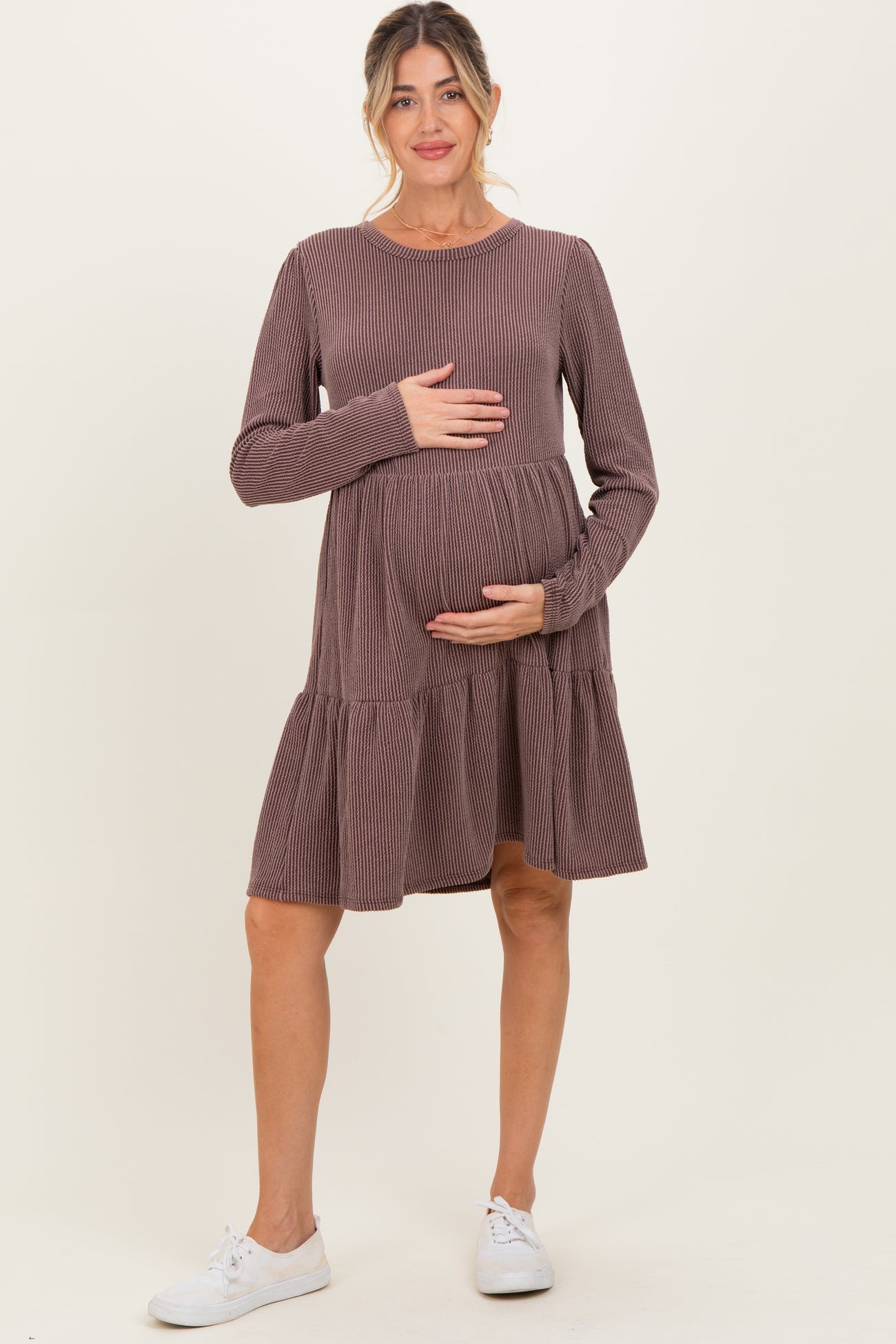 woman wearing a mauve ribbed long sleeve maternity dress with a tiered skirt and holding her baby bump