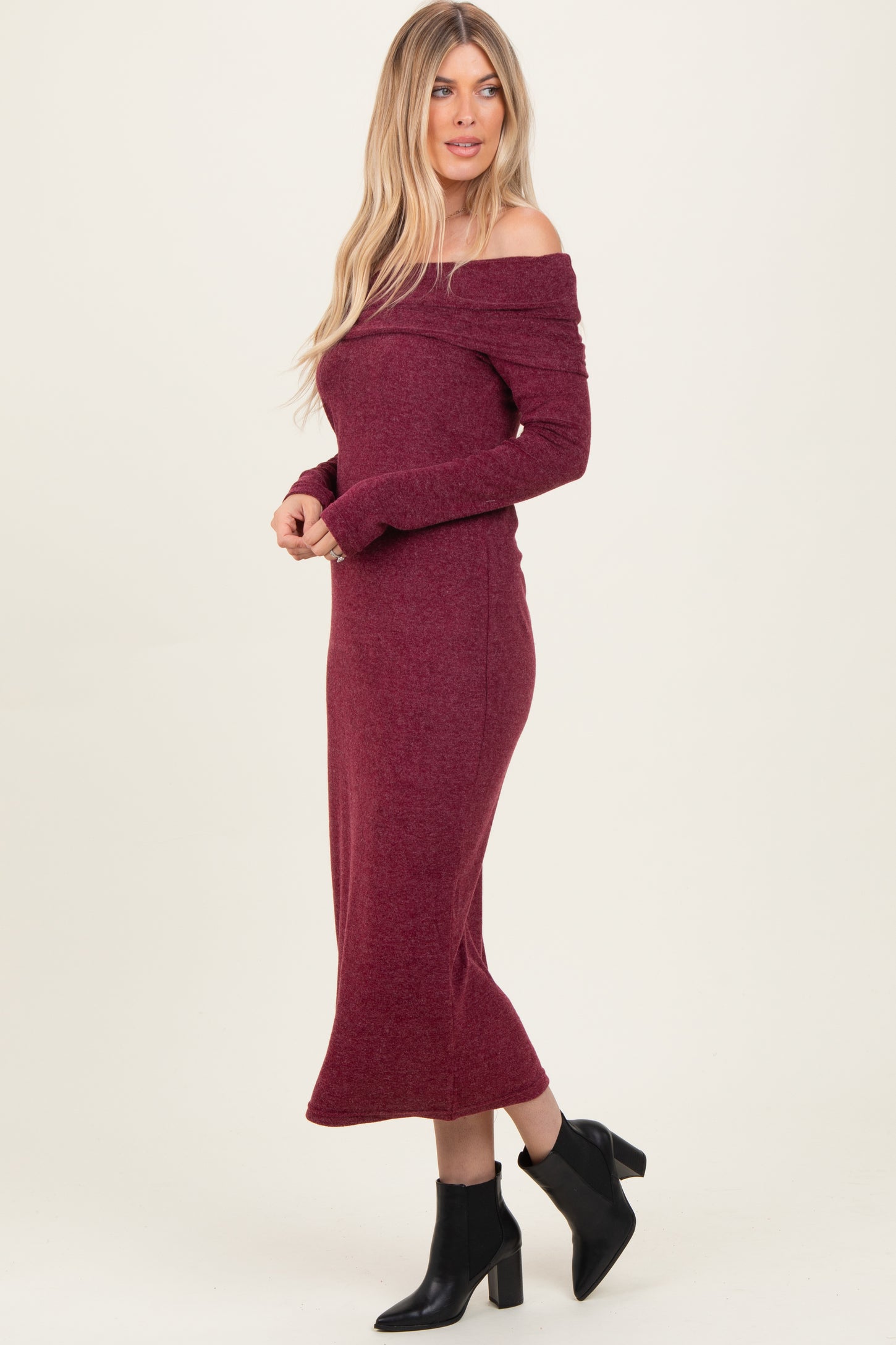 woman wearing a burgundy off-the-shoulder long sleeve midi dress paired with black ankle boots