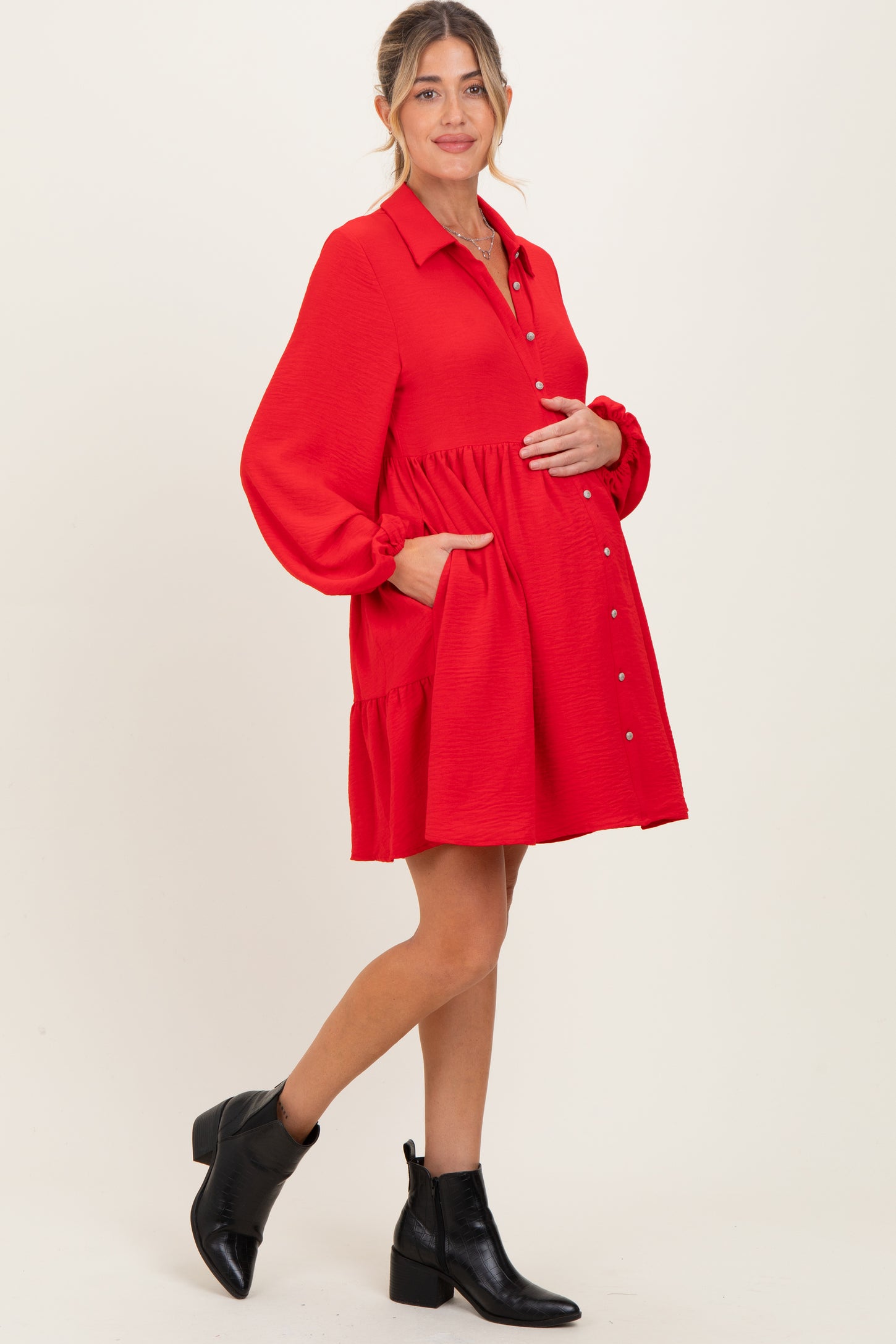 woman wearing a red maternity dress with a button-up front and pockets, showing her baby bump
