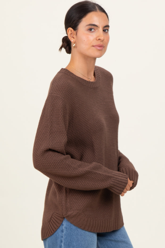 woman wearing a brown textured long sleeve sweater with side slits and relaxed fit, paired with blue jeans