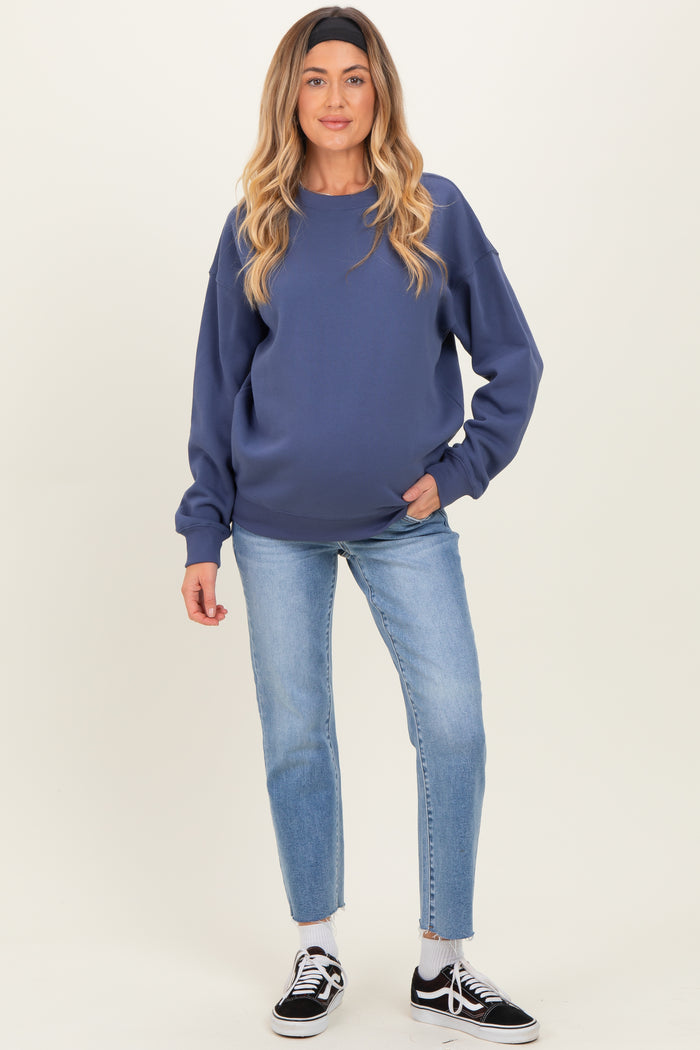 woman wearing a dark blue maternity sweatshirt and blue jeans, showing her baby bump, standing stylishly with a headband