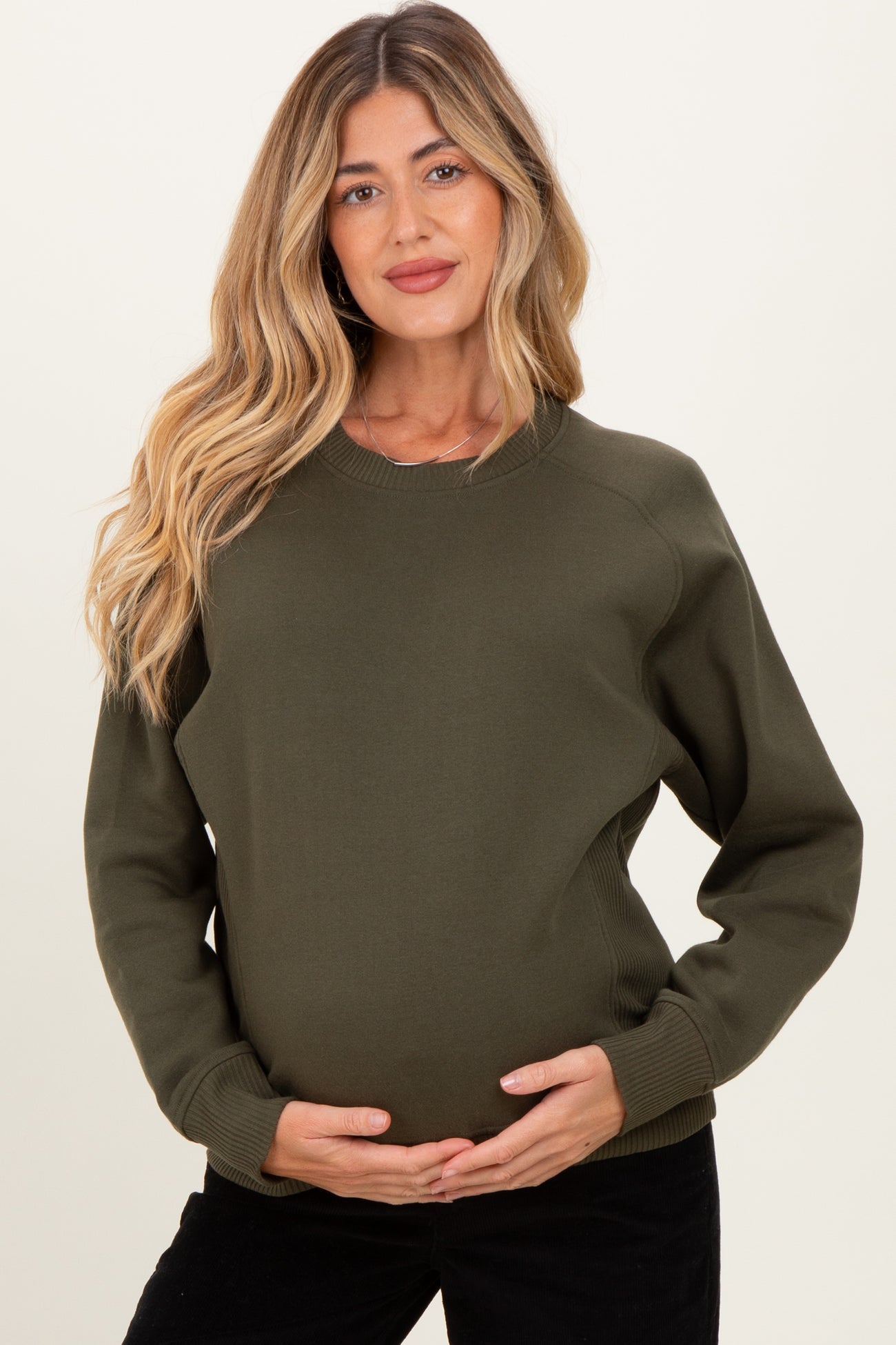 woman wearing an olive green maternity sweatshirt and holding her baby bump
