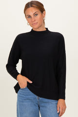 woman wearing a black mock neck sweater with dropped shoulders and side slits, paired with light blue jeans