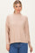 woman wearing a light beige oversized sweater with a high neckline and long sleeves, styled with blue jeans