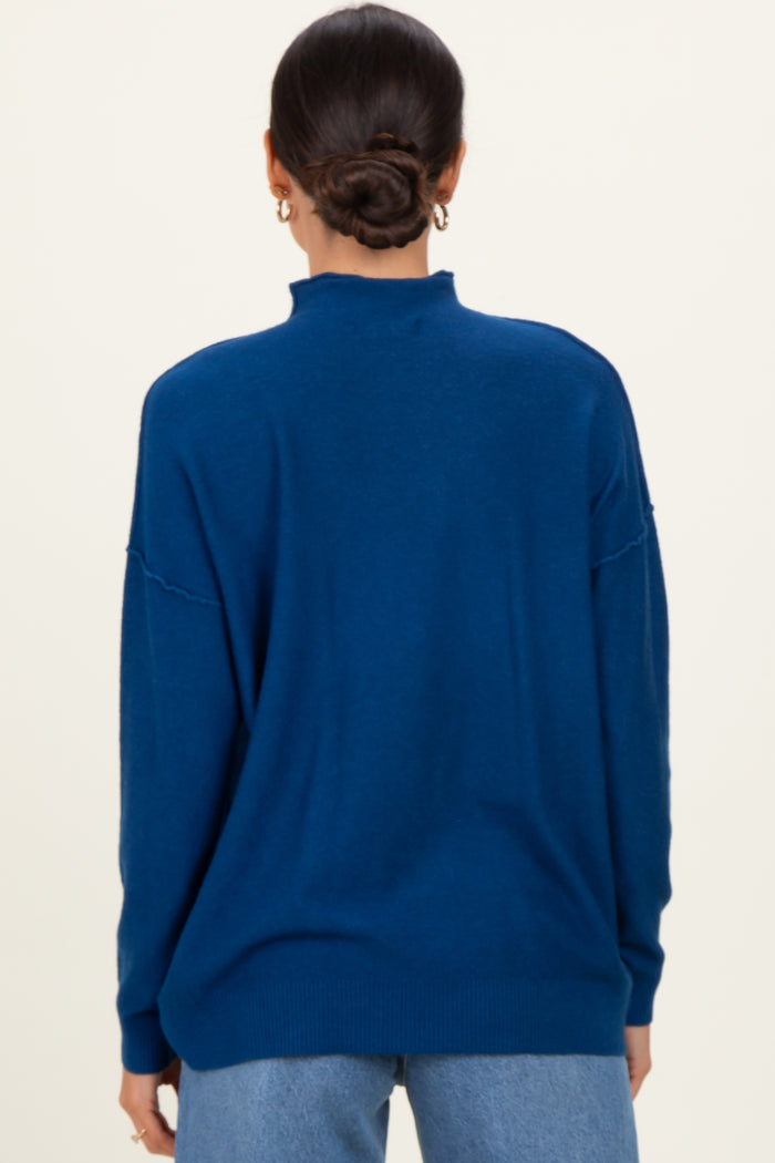 woman wearing a back view of a dark blue oversized sweater with a high neck and relaxed fit, styled with denim jeans