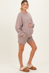 woman wearing a taupe maternity short set, holding her baby bump and standing in cozy slippers