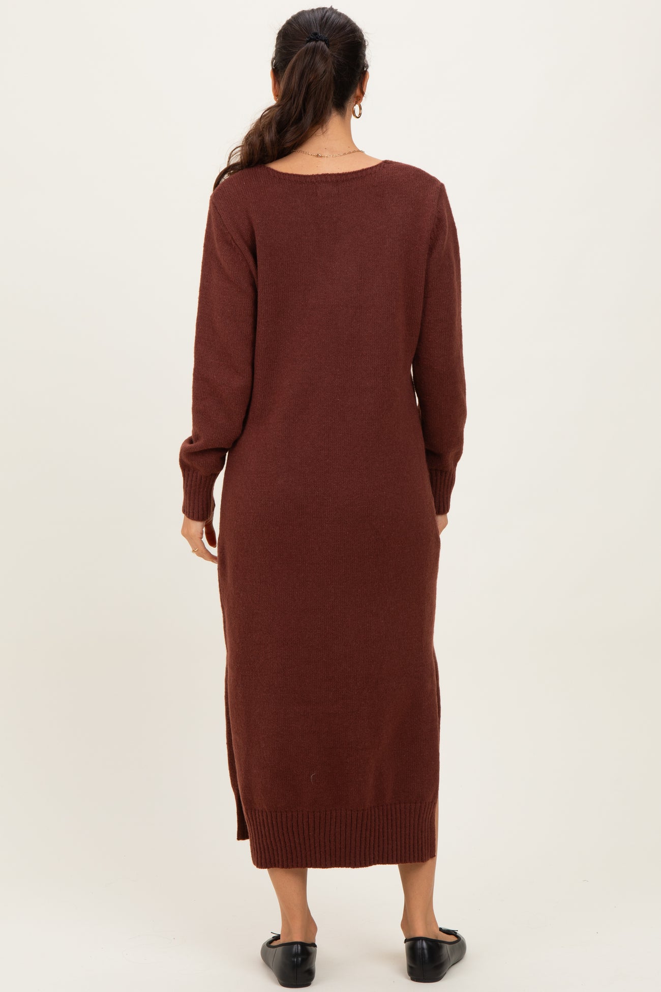 woman wearing a long brown sweater dress with long sleeves and side slits, viewed from the back