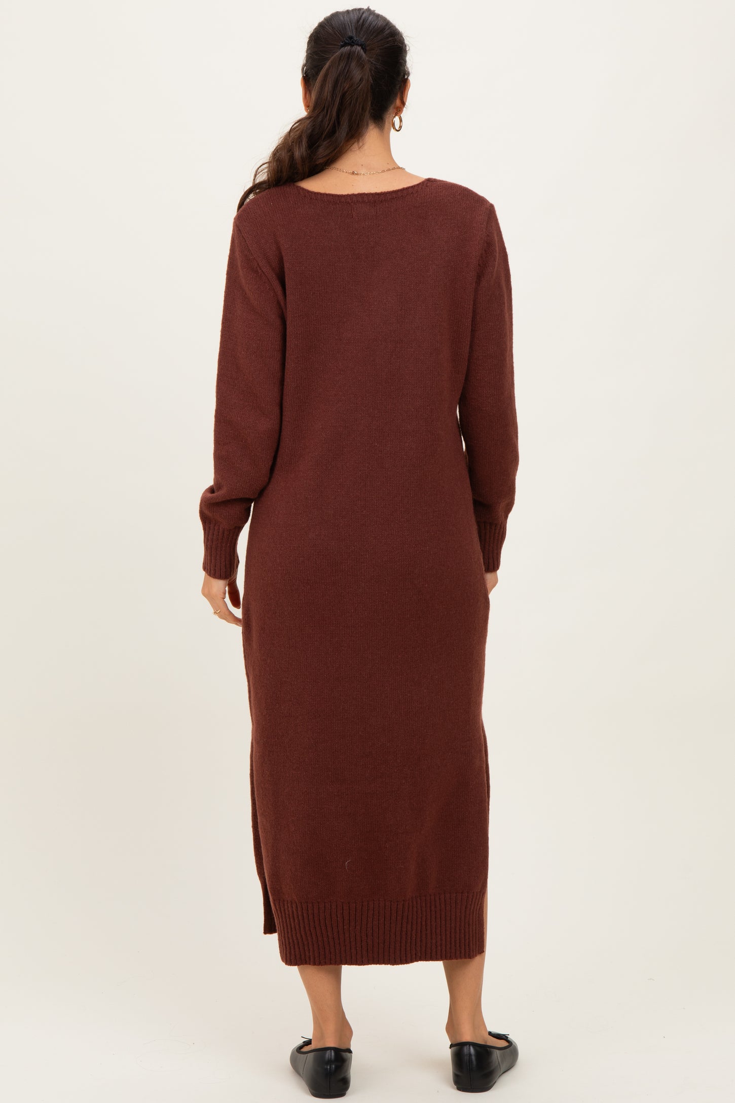 woman wearing a long brown sweater dress with long sleeves and side slits, viewed from the back