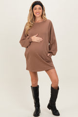 woman wearing a brown long sleeve maternity dress with pockets and holding her baby bump