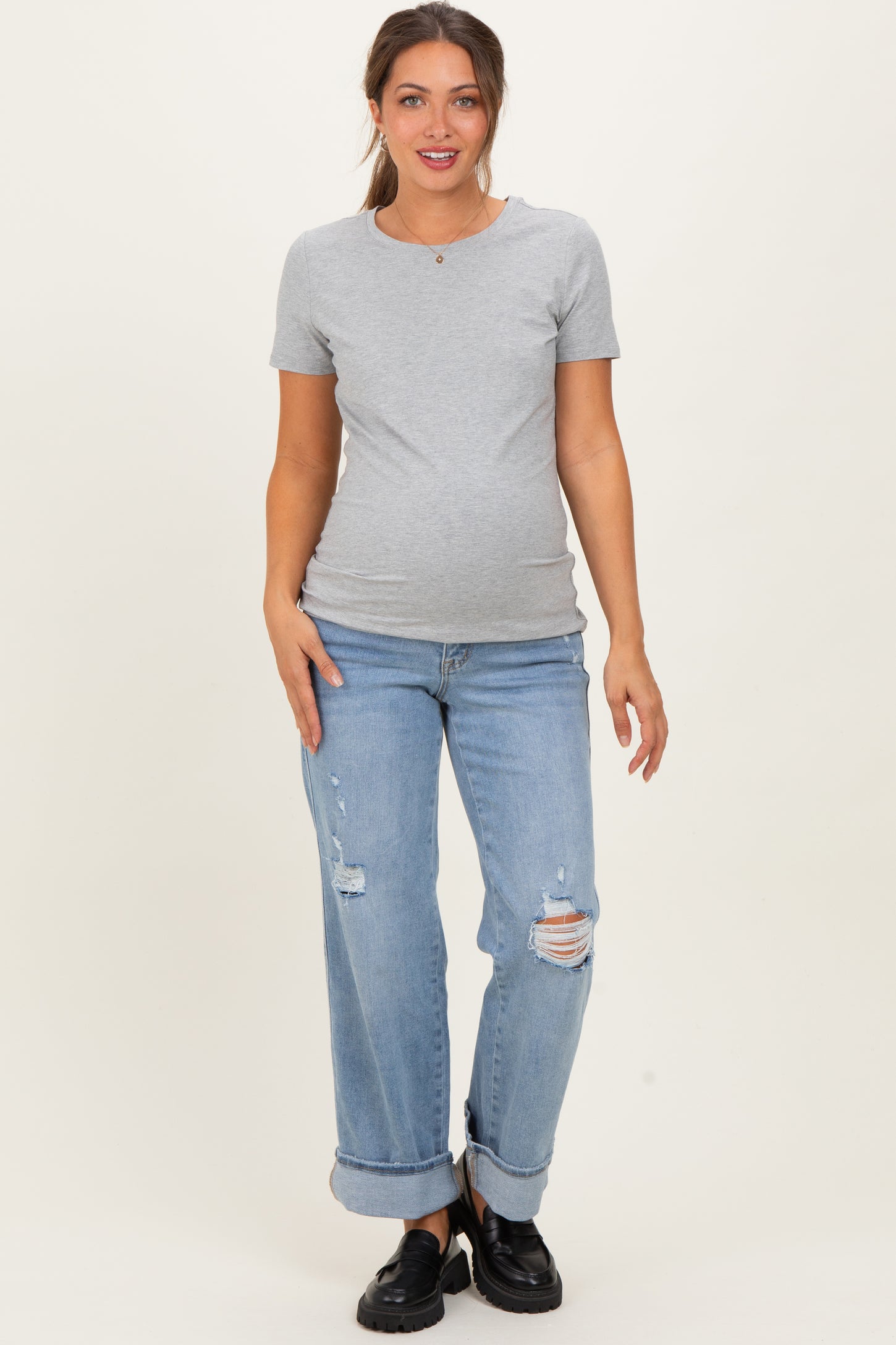 woman wearing a gray short sleeve maternity top and distressed light blue jeans, showing a visible baby bump