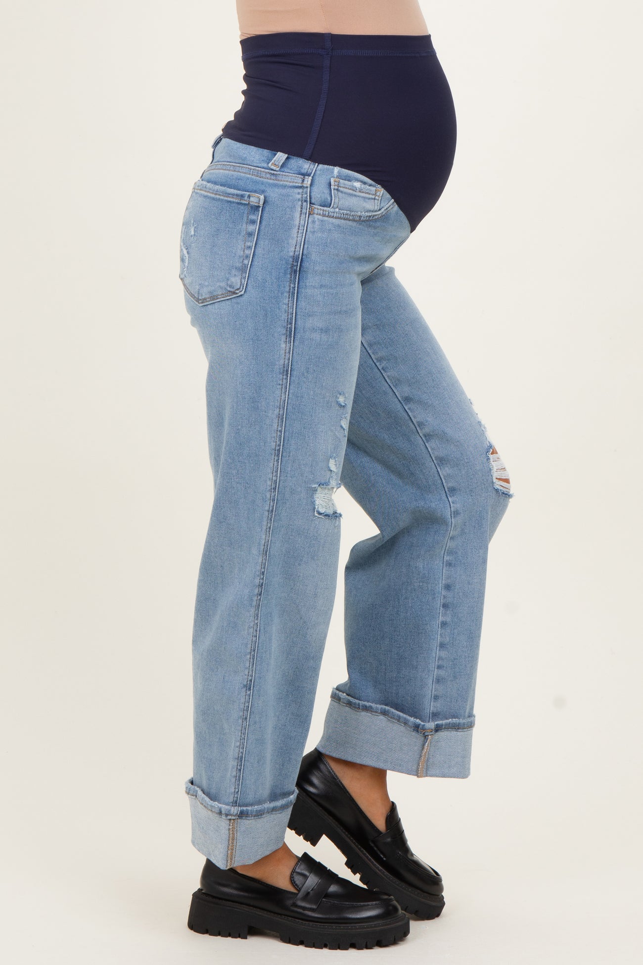 woman wearing maternity light blue distressed jeans with a dark blue belly band and black slip-on shoes, showing baby bump