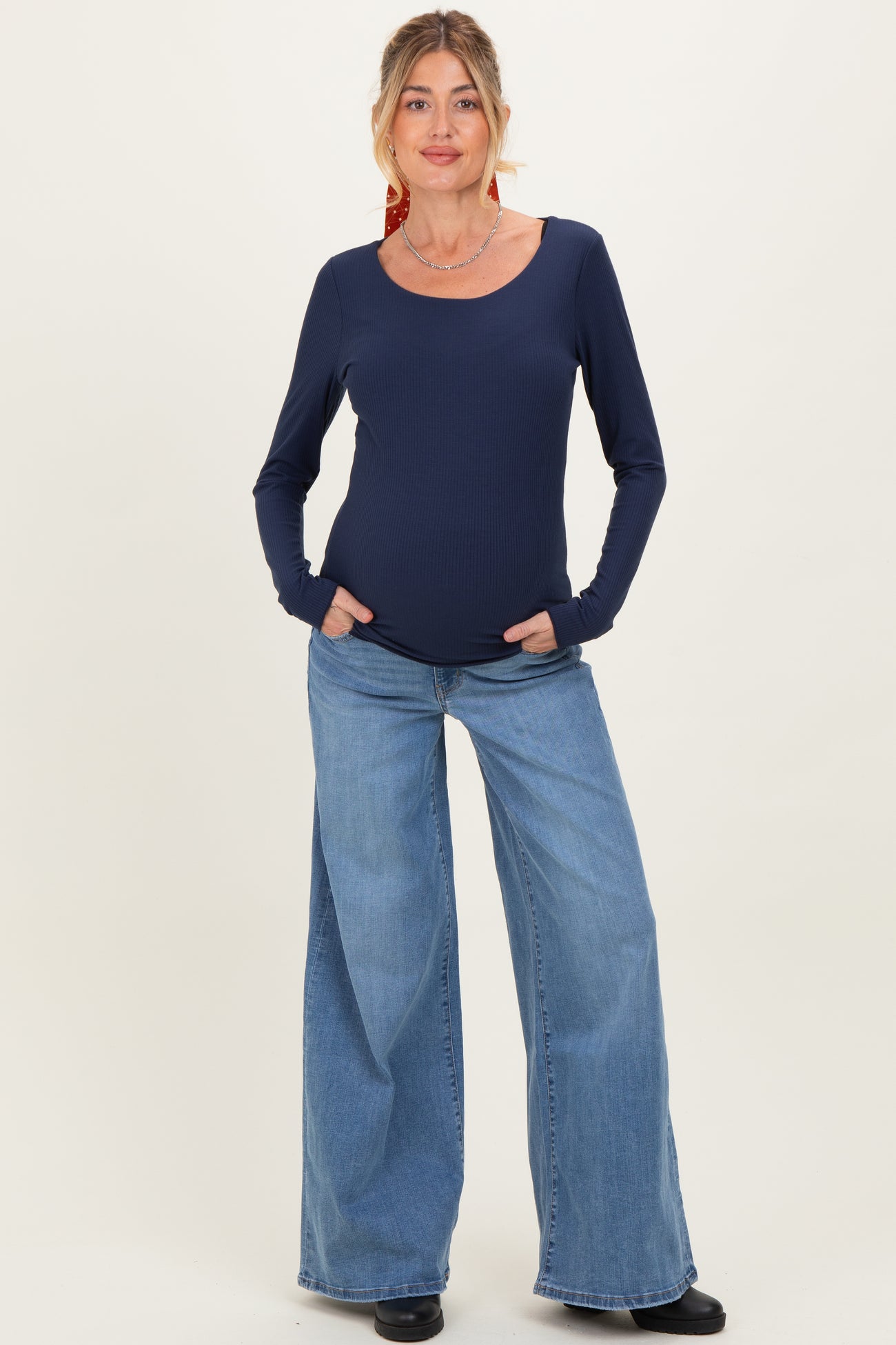 woman wearing a navy blue long sleeve maternity top with a scoop neckline and relaxed fit, paired with wide-leg jeans and posing with hands in pockets