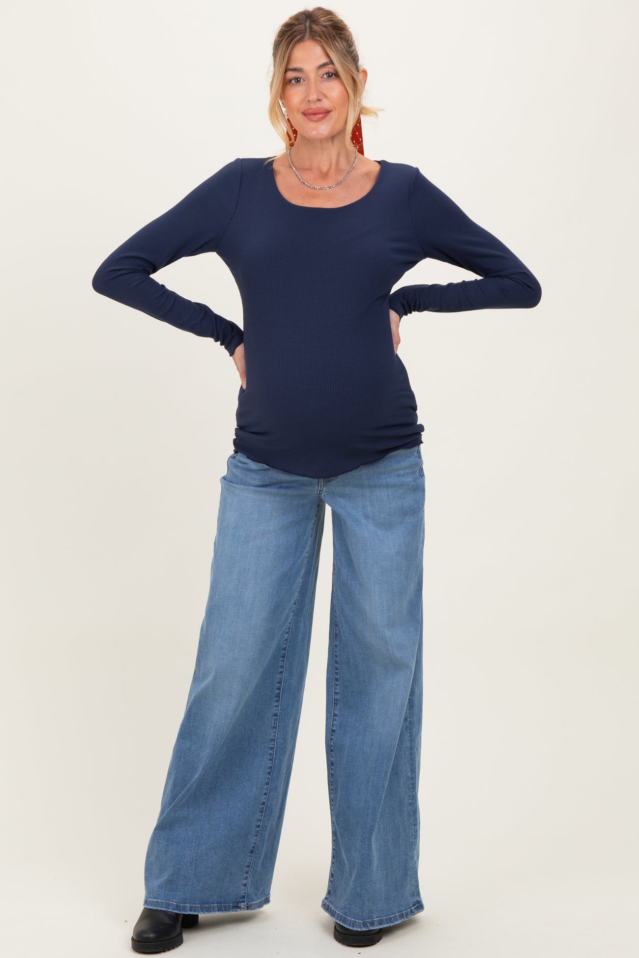 woman wearing a navy long sleeve maternity top and distressed wide leg jeans, showing her baby bump