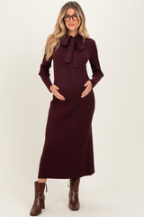 woman wearing a burgundy ribbed maternity dress with a bow tie detail and holding her baby bump