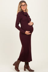 woman wearing a burgundy ribbed maternity dress with a bow detail, gently cradling her baby bump