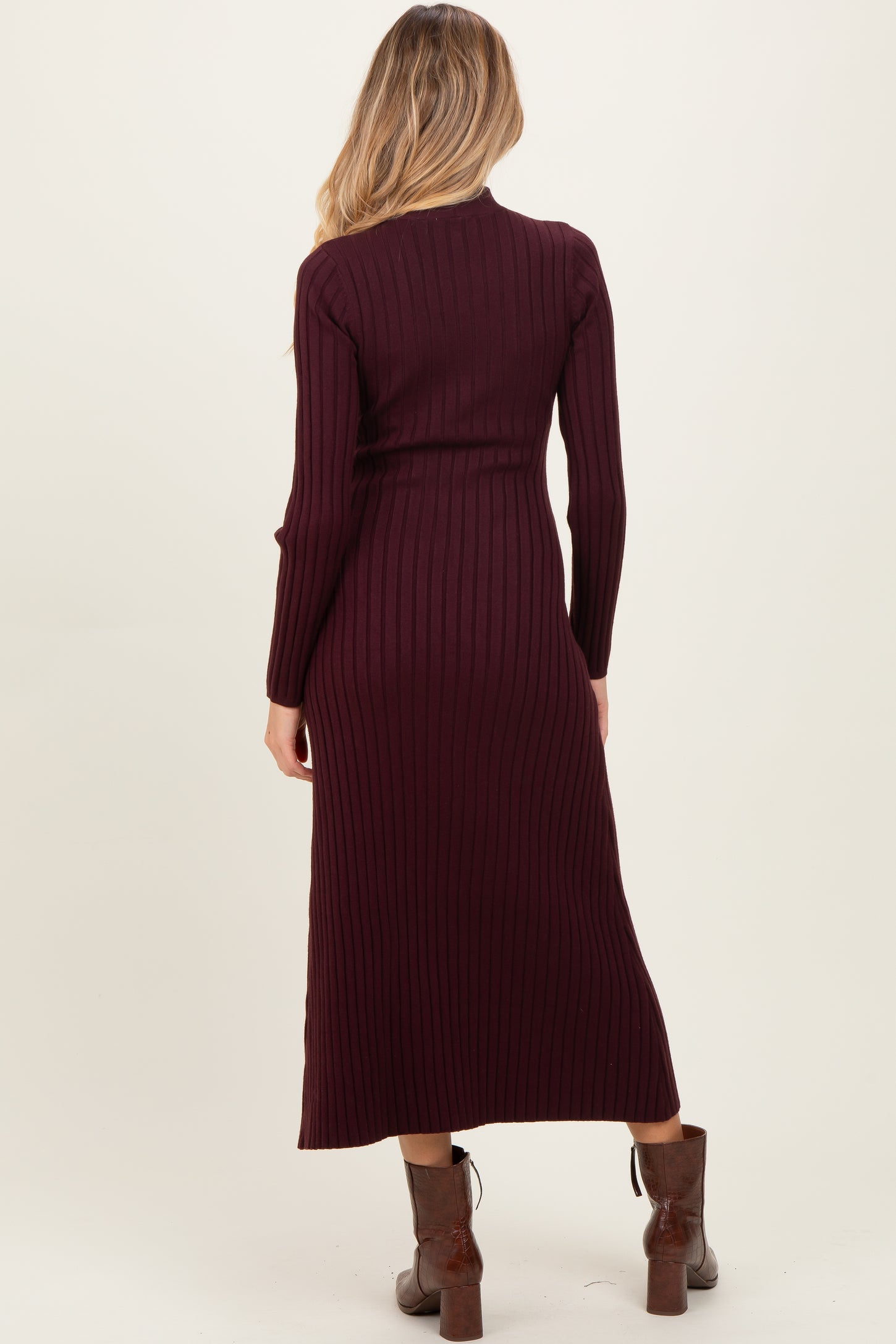 woman wearing a burgundy ribbed maternity dress with long sleeves and a fitted silhouette, showing a pregnant belly