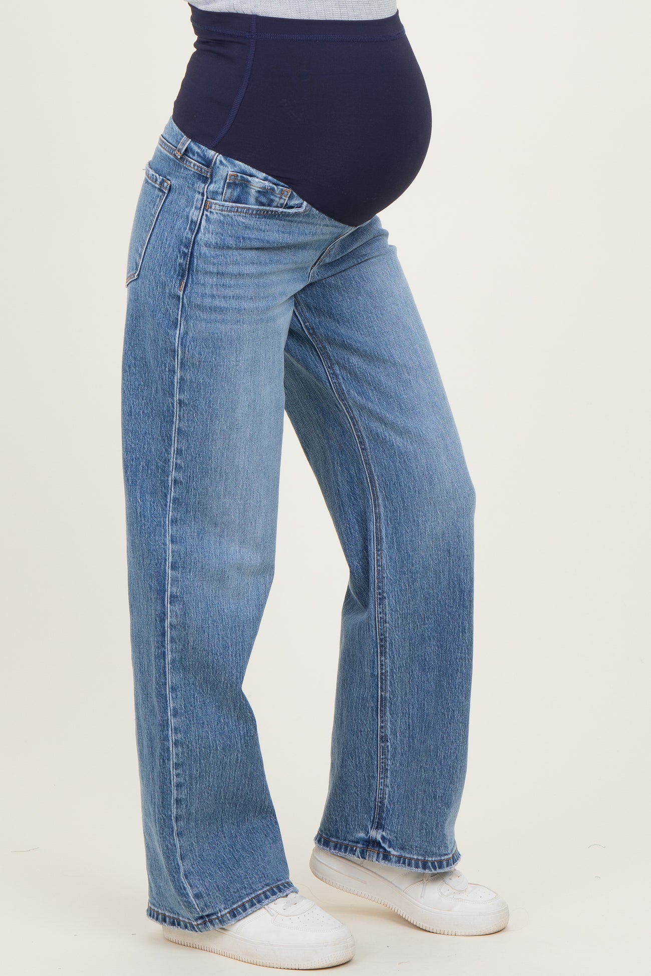 woman wearing light blue maternity jeans with a navy belly panel and standing with a baby bump visible
