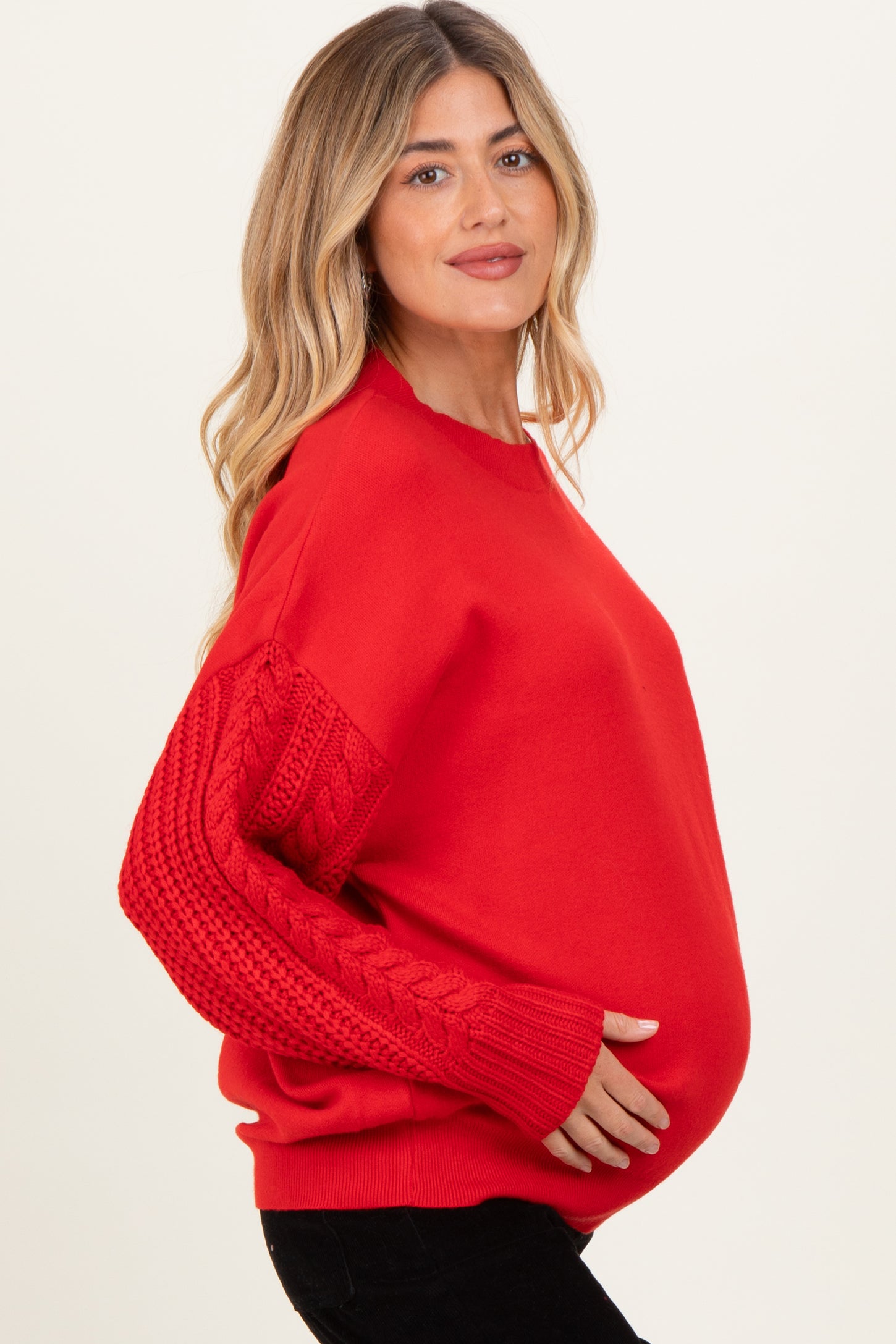 woman wearing a bright red maternity sweater with cable knit sleeves and a visible baby bump