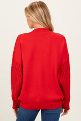 woman wearing a red oversized maternity sweater with textured knit sleeves and a relaxed fit from the back