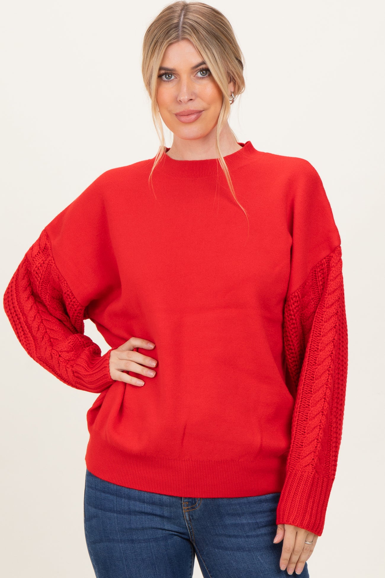 woman wearing a red oversized sweater with cable knit sleeves and a relaxed fit, paired with blue jeans