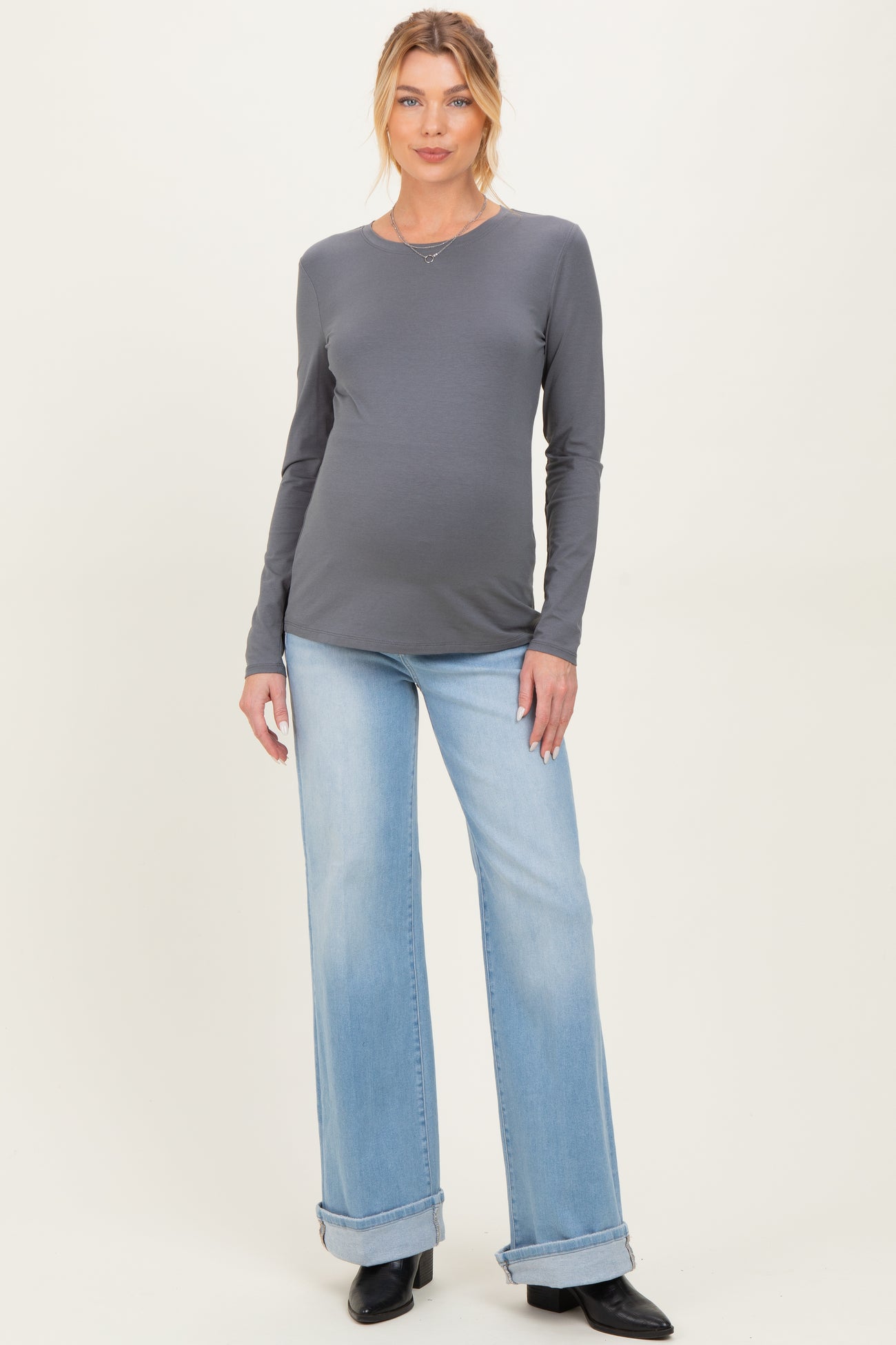 woman wearing a dark grey long sleeve maternity top and light blue flared jeans, showing her baby bump