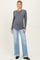 woman wearing a dark grey long sleeve maternity top and light blue flared jeans, showing her baby bump