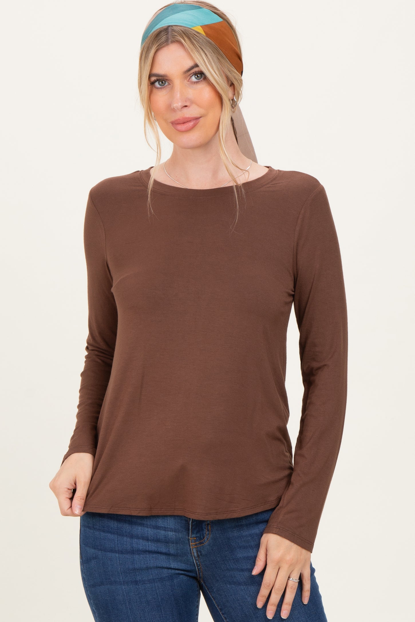 woman wearing a brown long sleeve top with a scoop neckline and denim jeans, styled with a headscarf