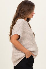 woman wearing a light beige short sleeve maternity sweater with a loose fit and side pockets, showcasing her baby bump