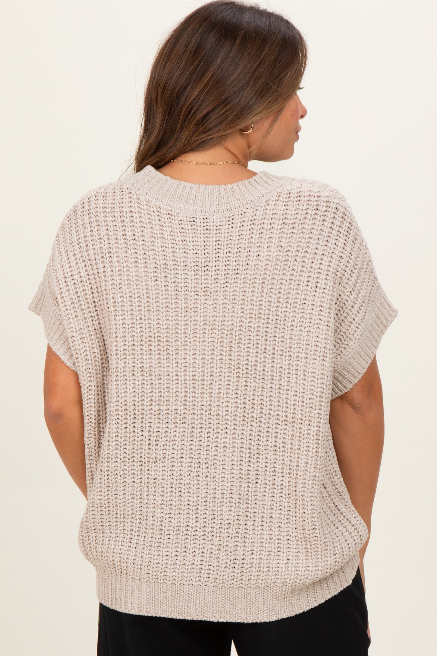 woman wearing a beige loose-knit maternity sweater with short sleeves and a relaxed fit seen from the back