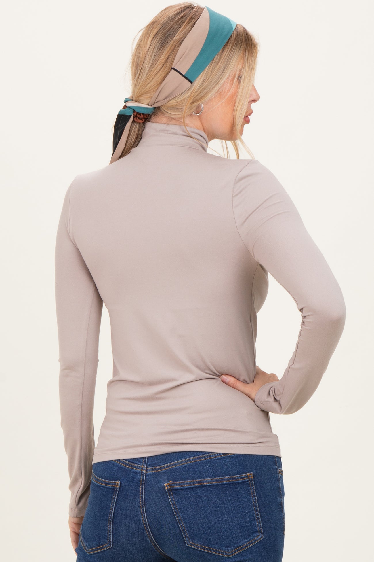 woman wearing a taupe long sleeve mock neck top paired with blue jeans, view from the back