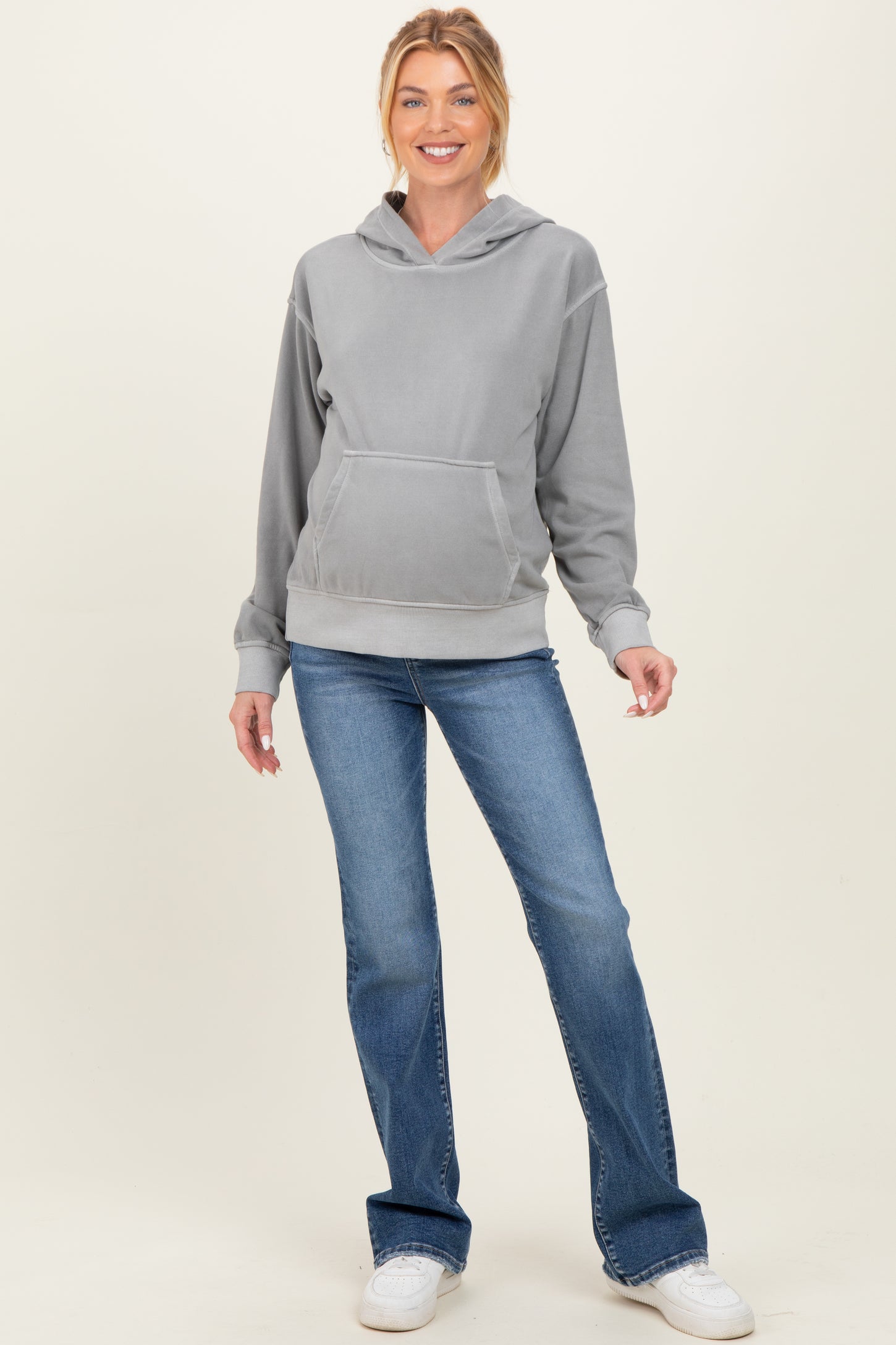 woman wearing a gray maternity hoodie with a front pocket and blue maternity jeans, styled casually with sneakers