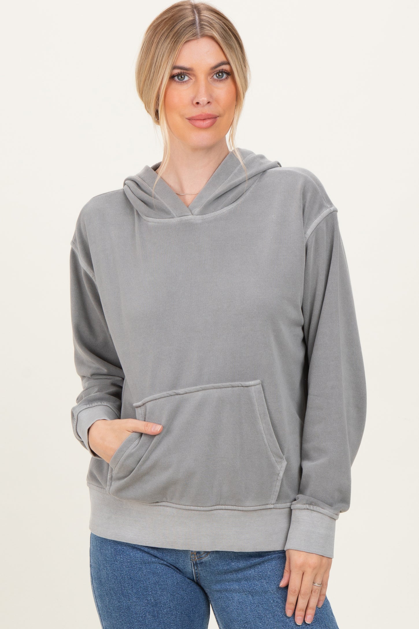 woman wearing a gray oversized hoodie with a front pocket and drawstring hood, styled with blue jeans