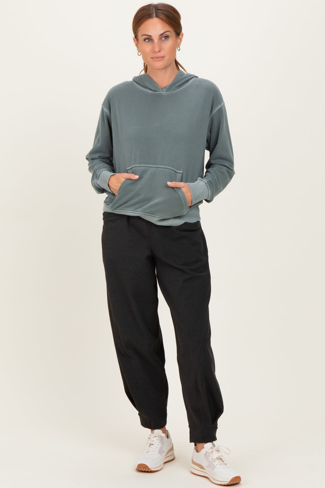 woman wearing a green hooded sweatshirt with a front pocket and black jogger pants, paired with white sneakers
