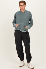 woman wearing a green hooded sweatshirt with a front pocket and black jogger pants, paired with white sneakers