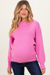woman wearing a bright pink ribbed maternity sweater with a round neckline and loose-fitting sleeves, showing her baby bump