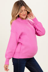 woman wearing a bright pink oversized maternity sweater with a ribbed texture and a relaxed fit, showing her baby bump