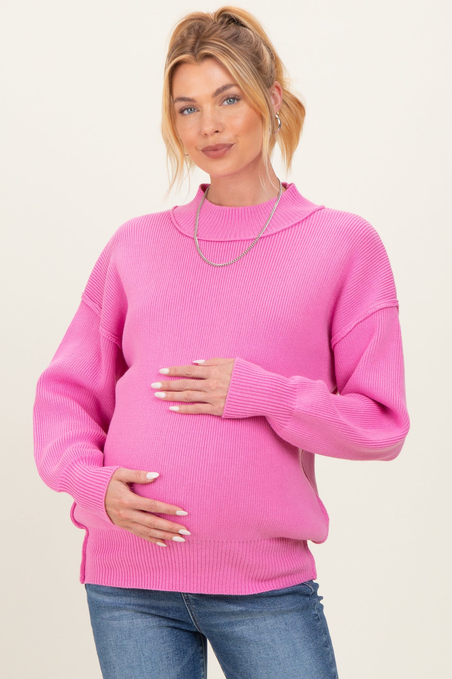woman wearing a bright pink maternity sweater and holding her baby bump