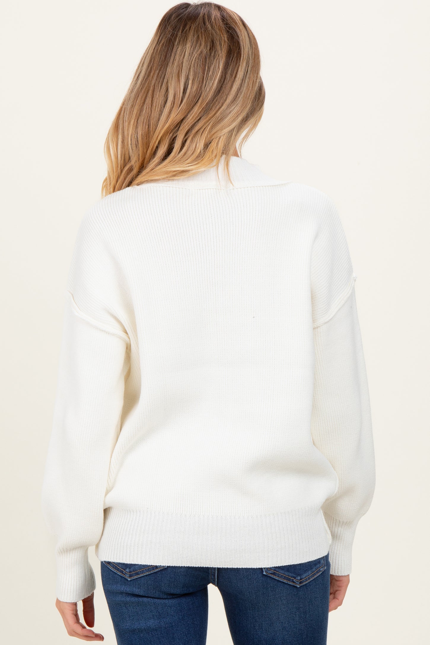 woman wearing a white oversized maternity sweater, showing the back view with relaxed fit and ribbed details