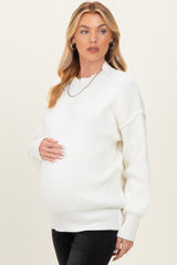 woman wearing a white ribbed maternity sweater and holding her baby bump