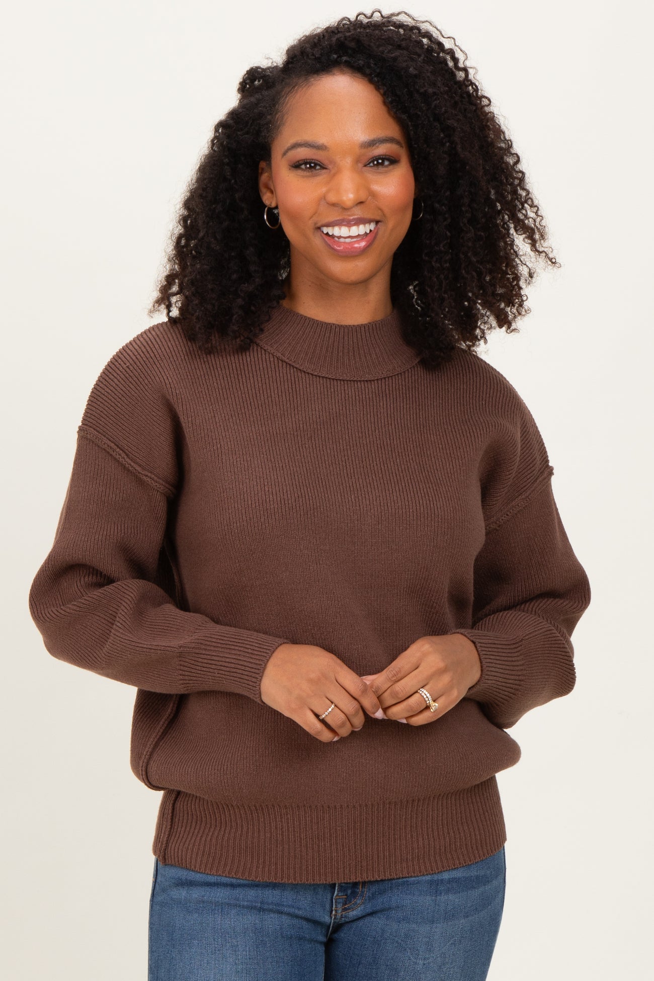 woman wearing a brown oversized sweater with a ribbed neckline and cuffs, smiling at the camera