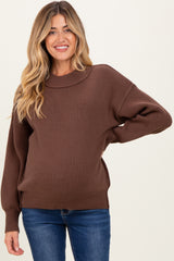 woman wearing a brown maternity oversized sweater and showing her baby bump