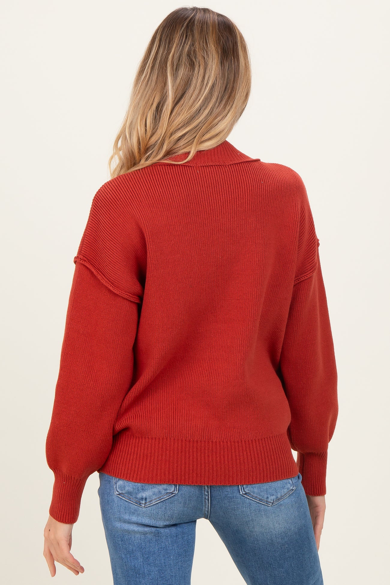 woman wearing a rust-colored maternity sweater with balloon sleeves and ribbed detailing, shown from the back