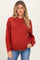 woman wearing a rust-colored knitted maternity sweater with a relaxed fit and long sleeves, showing baby bump